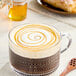 A glass of coffee with a swirly caramel top next to a jar of Hometown Provisions Wildflower Honey.