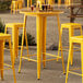 A Lancaster Table & Seating 30" Round Citrine Yellow Bar Height Outdoor Table with yellow bar stools on an outdoor patio.