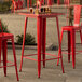 A Lancaster Table & Seating ruby red metal bar table with chairs on an outdoor patio.