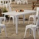 A Lancaster Table & Seating pearl white table on a patio with white chairs.