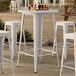A Lancaster Table & Seating white bar table set with white chairs.