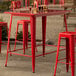 A red metal bar table with red stools on an outdoor patio.