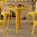 A Lancaster Table & Seating citrine yellow metal table and chairs set up on an outdoor patio.