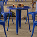 A Lancaster Table & Seating blue metal table with legs on an outdoor patio.