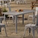 A Lancaster Table & Seating Alloy Series nickel gray table with legs and chairs on an outdoor patio.