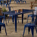 A Lancaster Table & Seating sapphire blue metal table with blue chairs on an outdoor patio.