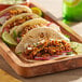 A plate of tacos with BE Hive plant-based beef crumbles, lettuce, and cheese on a table.