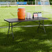 A black heavy-duty blow molded plastic folding table with black legs set up on a sports field.