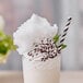 A glass of milkshake with whipped cream and green cotton candy on top.