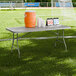 A gray heavy-duty blow molded plastic folding table with gray legs set up on a sports field.