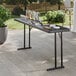A black heavy-duty blow molded plastic folding table with black legs, set up outdoors with drinks and snacks on top.