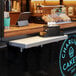A Regency aluminum folding concession shelf mounted on a wall above a counter with a tray of pastries.