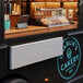 A Regency aluminum folding concession shelf mounted on a white wall in a food truck interior with a laptop and pastries.