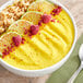 A white bowl filled with yellow smoothie with fruit slices and oatmeal with a spoon.