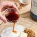 A person pouring Hometown Provisions Imitation Vanilla into a bowl of brown liquid.