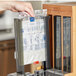 A hand using a World Centric TPLA knife refill sleeve in a professional kitchen to fill a paper dispenser.