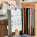 A hand holding a World Centric TPLA Spoon Refill sleeve bag on a kitchen counter.