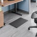 A black rectangular anti-fatigue mat placed on the floor near a standing desk in an office setting.