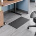 A black rectangular anti-fatigue standing desk mat placed on an office floor.
