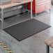 A black 4' x 6' grease-resistant anti-fatigue closed-cell nitrile rubber floor mat with beveled edges, placed on a workshop floor.
