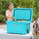 A woman in a blue outdoor patio opening a CaterGator sky blue cooler to put bottles inside.