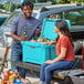 A man and woman sitting on the back of a truck with a CaterGator sky blue cooler full of beer.