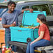 A man and woman sitting on the back of a CaterGator cooler.