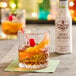 A glass of whiskey with a cherry and a straw next to a bottle of Fee Brothers Mole Bitters.