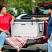 A man and woman sitting on the back of a truck holding a black CaterGator cooler.