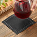 A hand holding a glass of red wine over a black Choice cloth napkin.
