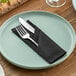 A black cloth napkin with a fork and knife on a plate.