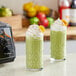 Two glasses of green smoothie with whipped cream and bananas on a counter.