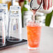 A hand pouring orange liquid into an Acopa Endure Tritan mixing glass with ice.