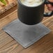 A hand holding a black mug with foam above a gray Choice cloth napkin.