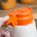 A hand holding a Tablecraft orange plastic dressing lid over a clear plastic container.