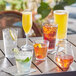 Acopa Endure Tritan plastic stackable rocks glasses filled with various drinks on a table.