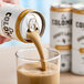 A hand pours La Colombe Caramel Draft Latte into a glass.