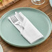 A fork and knife on a white napkin on a plate.
