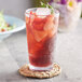 A stackable Acopa Tritan highball glass filled with a red drink, ice, and strawberries with a straw.