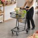 A woman pushing a Regency black shopping cart full of groceries.