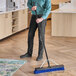 A man using a Lavex Polypropylene Push Broom with a squeegee attachment and metal handle to sweep a floor in a professional kitchen.