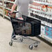 A man using a Regency black plastic grocery cart to shop in a grocery store.