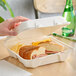 A hand holding a sandwich in a Fabri-Kal Greenware 3-compartment hinged container.