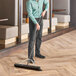 A man using a Lavex polypropylene push broom with steel brace and flagged bristles to sweep a floor.