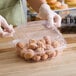 A person in gloves putting donuts in a Choice clear hinged plastic container.