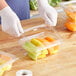 A person wearing white gloves cutting up fruit and placing it in an Inline Plastics rectangular plastic container with a flat lid.