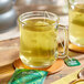 A glass mug of Pukka Organic Supreme Matcha Green Tea on a wooden table with a spoon.