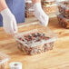 A person in gloves holding a Inline Plastics clear plastic container of nuts and dried fruits.