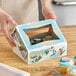 A person holding a Southern Champion cookie box with a window and a snowman on it.