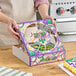 A woman holding a Southern Champion bakery box with a Mardi Gras King Cake design containing a cake.